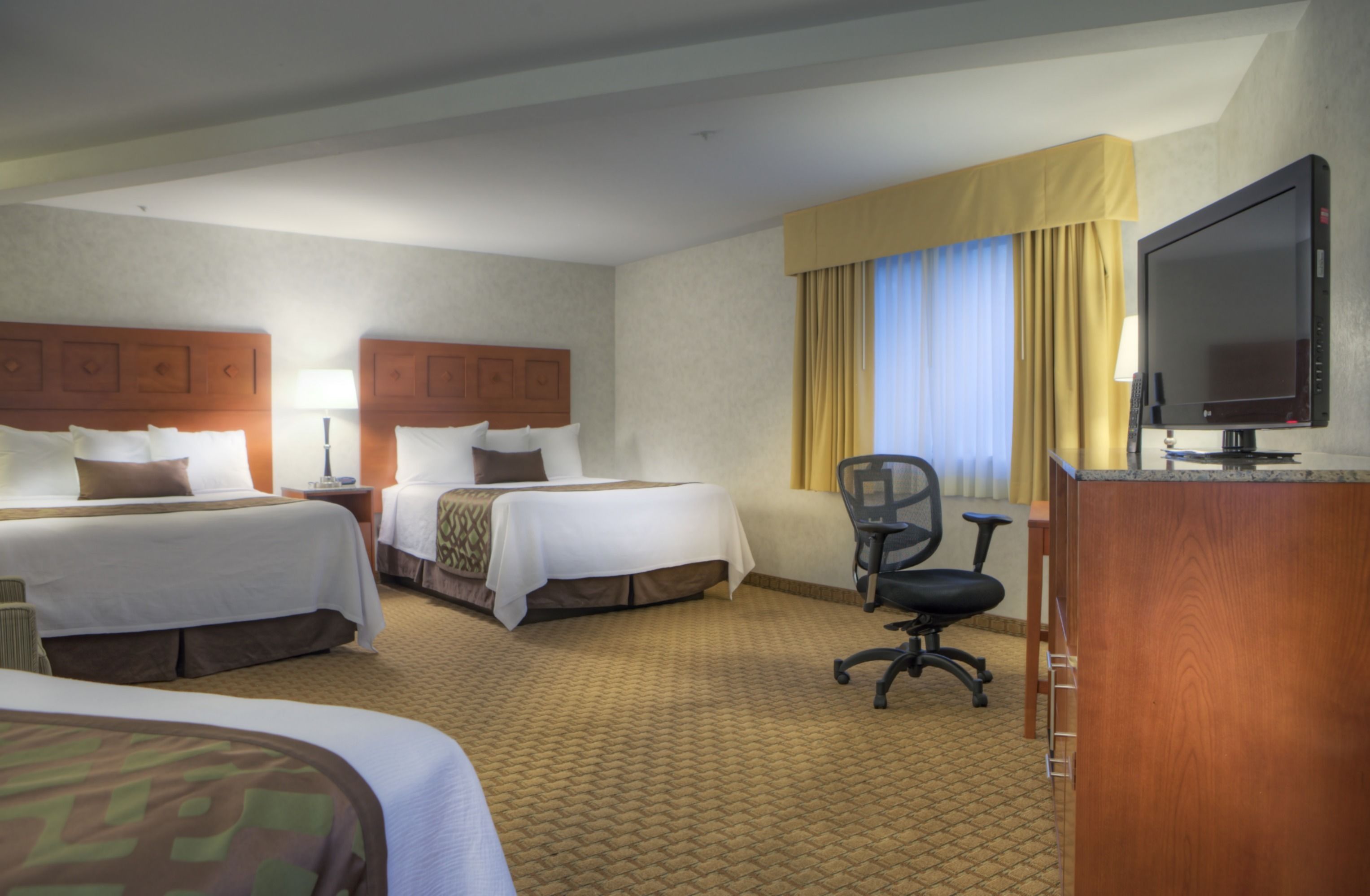 A hotel room with two beds, a desk with a chair, a television, and a window with curtains.