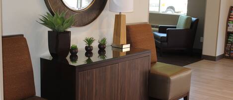 A reception area with a dark wood cabinet, a mirror, a potted plant, and two leather chairs.