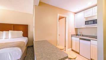Une chambre d’hôtel comprenant un lit, une petite table, un coin cuisine avec un four à micro-ondes et un lave-vaisselle.