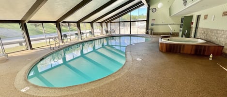Una amplia piscina cubierta con vistas a un campo de golf a través de grandes ventanales.