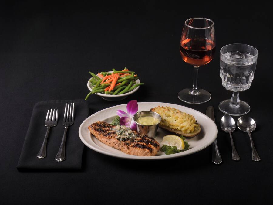 A plate with salmon, a bowl of green beans, and a glass of water on a black table.