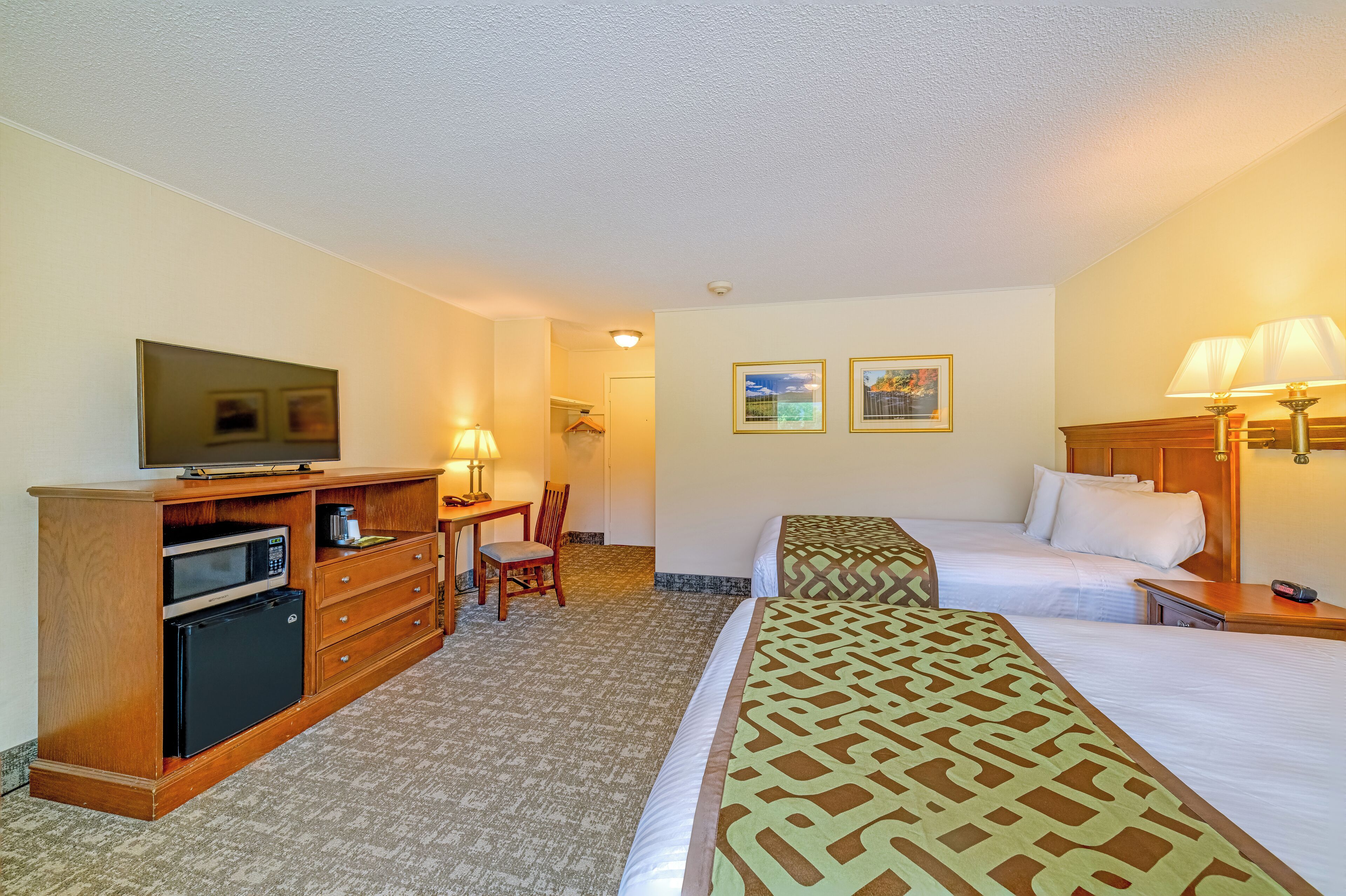 A hotel room with a bed, a desk with a lamp, a television, a microwave, and a refrigerator.