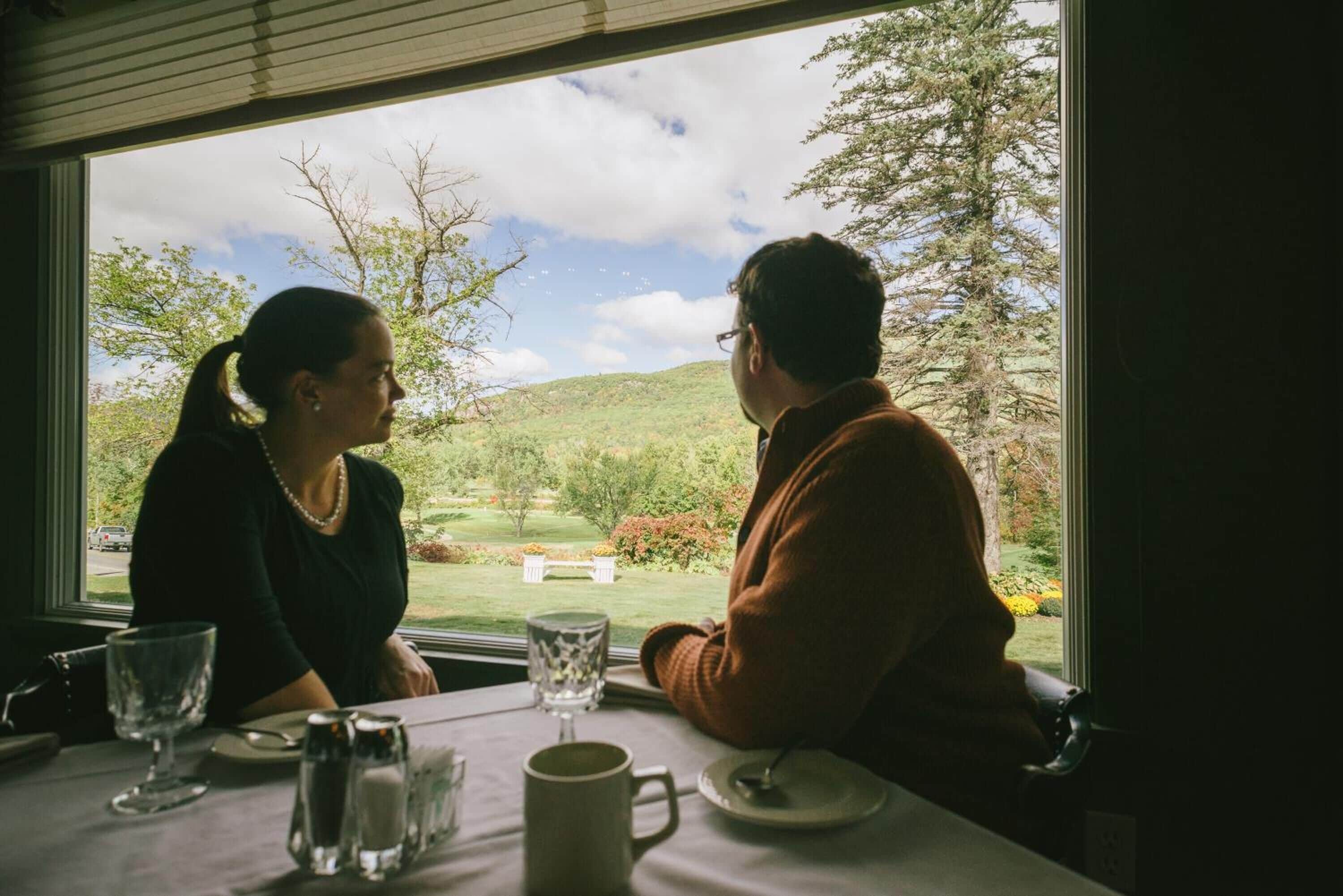 Deux personnes sont assises à une table, devant un paysage verdoyant et des collines.