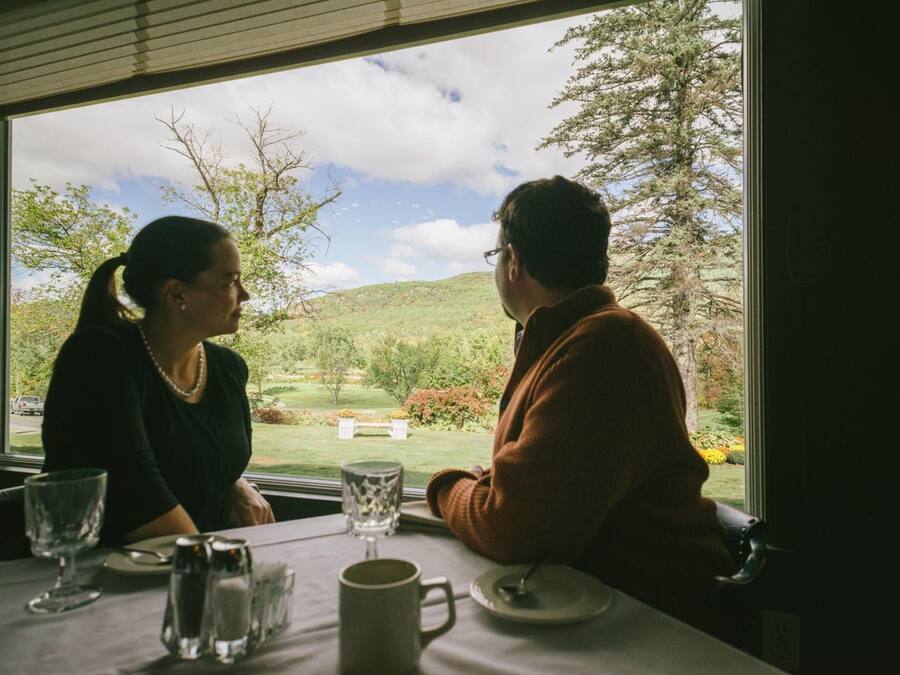 Deux personnes sont assises à une table, devant un paysage verdoyant et des collines.