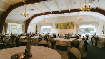 A banquet hall with round tables, black and white chairs, chandeliers, and a large painting on the wall.