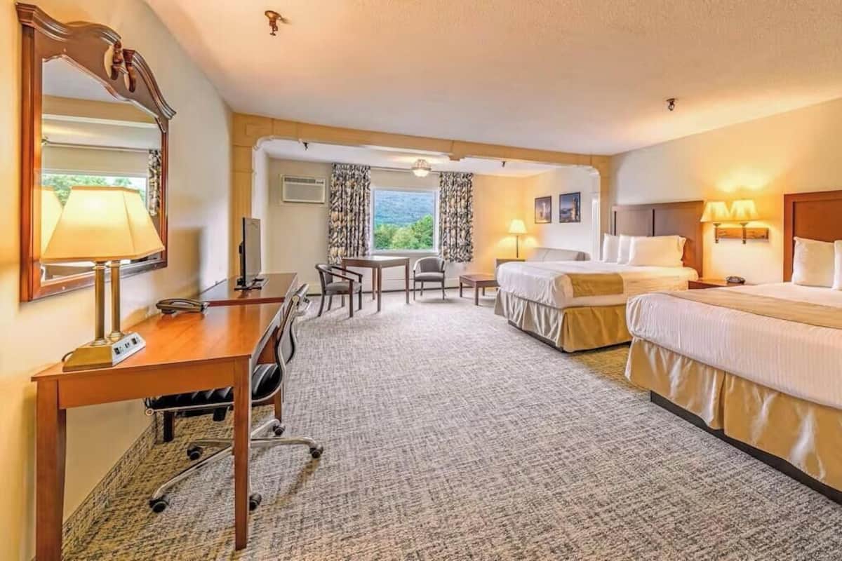 A hotel room with two beds, a desk, a chair, a lamp, and a large mirror.