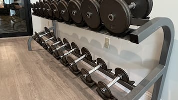 Et fitnessrum med styrketræningsudstyr, herunder håndvægte og vægtstænger, arrangeret på et stativ.