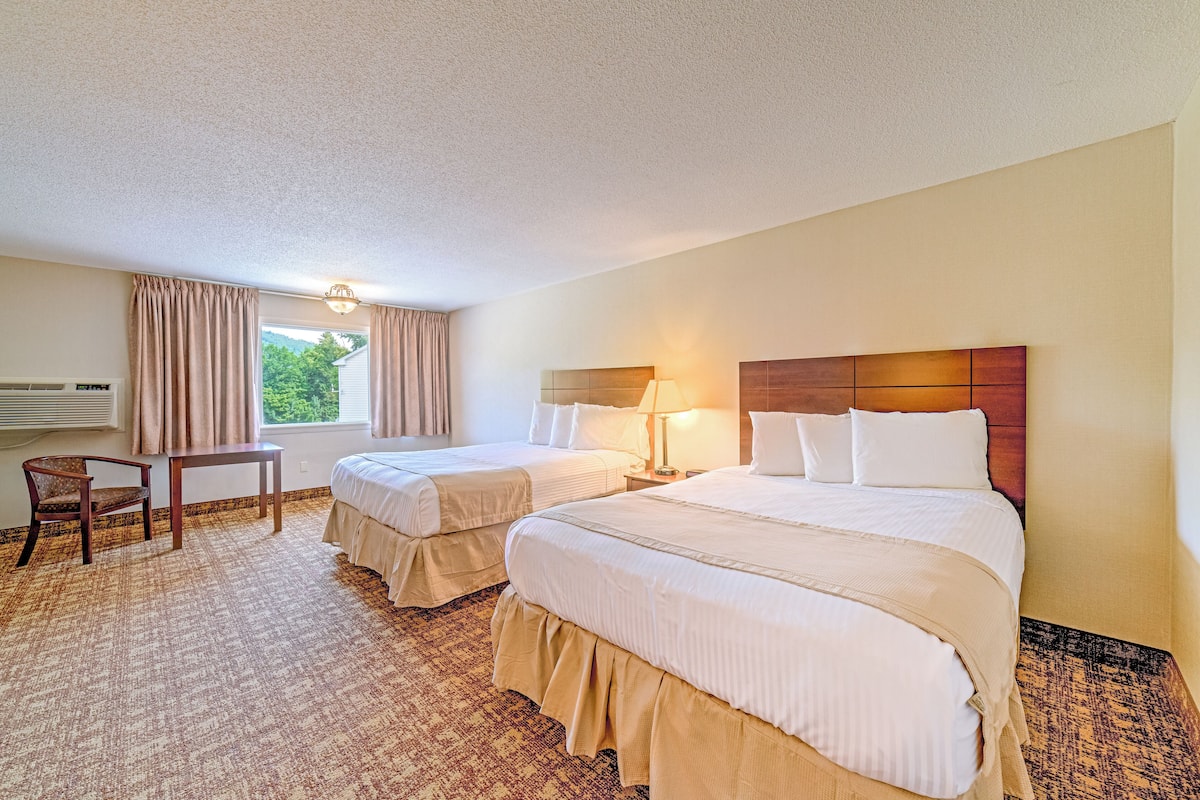 A hotel room with two beds, a chair, a table, and a window with curtains.