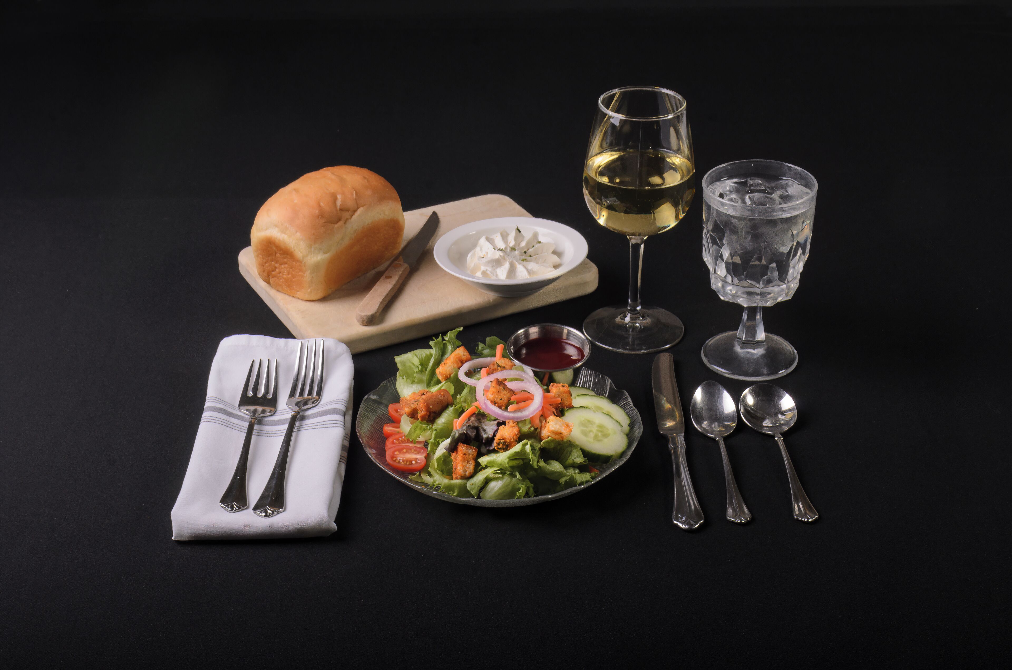Comida con pan, ensalada y bebidas sobre una mesa.