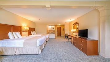 Une chambre d’hôtel avec deux lits, un bureau avec une télévision et une salle de bain visible à travers une porte ouverte.
