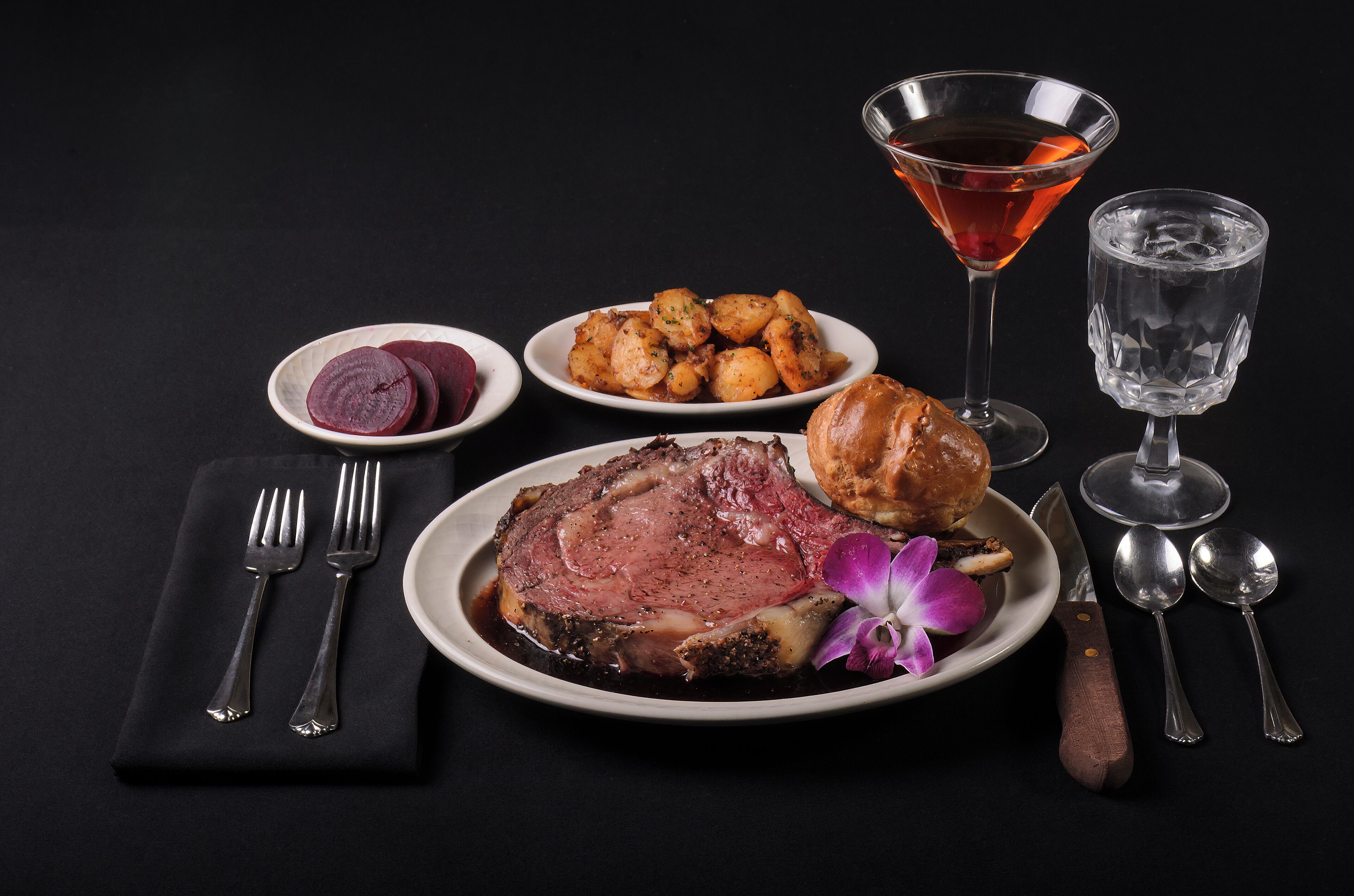 A dinner setting with a steak, roasted potatoes, and a martini glass.