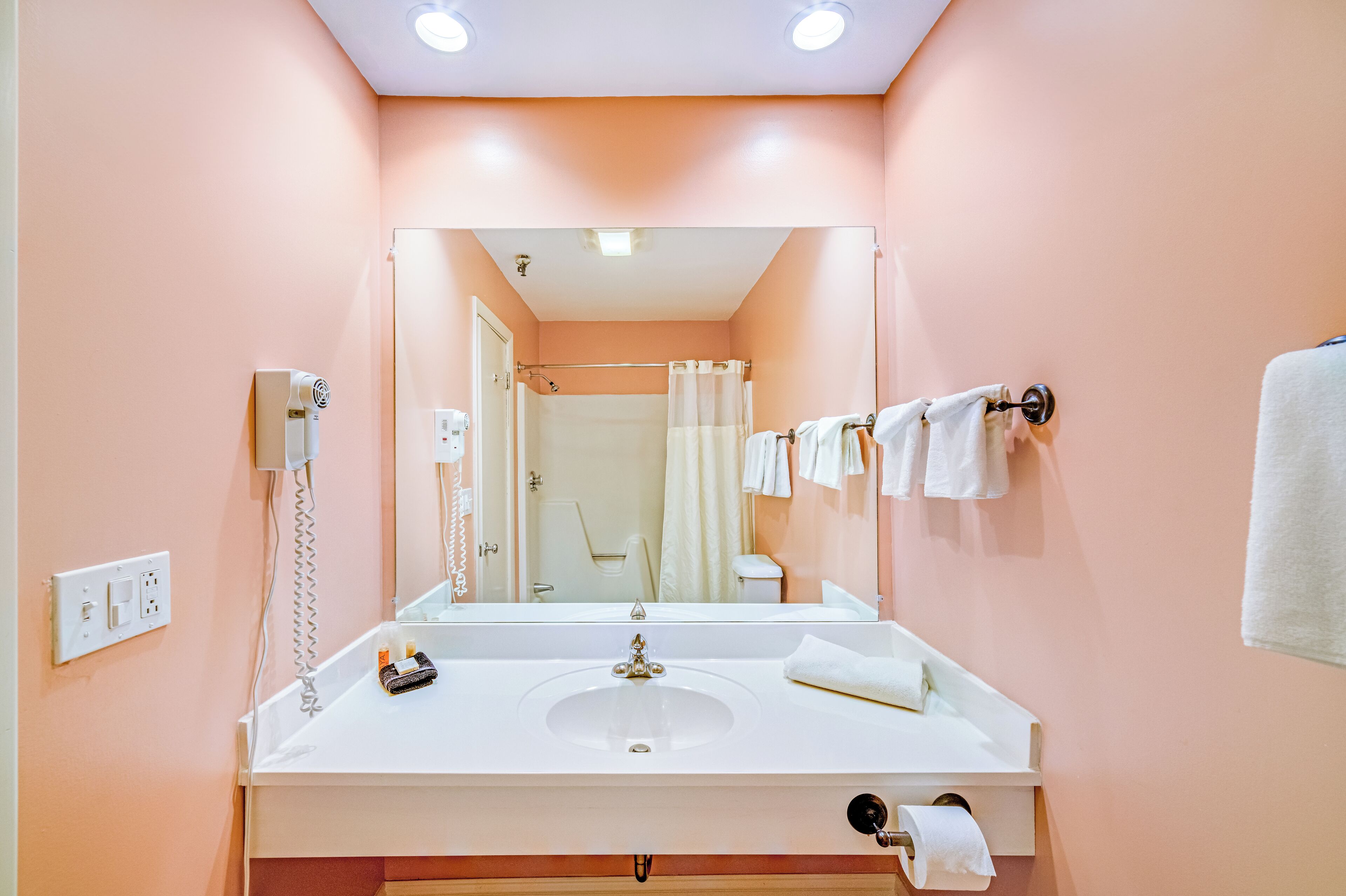 Un baño con un lavamanos blanco, un espejo, una cortina de ducha y toallas colgadas en un perchero.