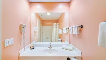 Un baño con un lavamanos blanco, un espejo, una cortina de ducha y toallas colgadas en un perchero.