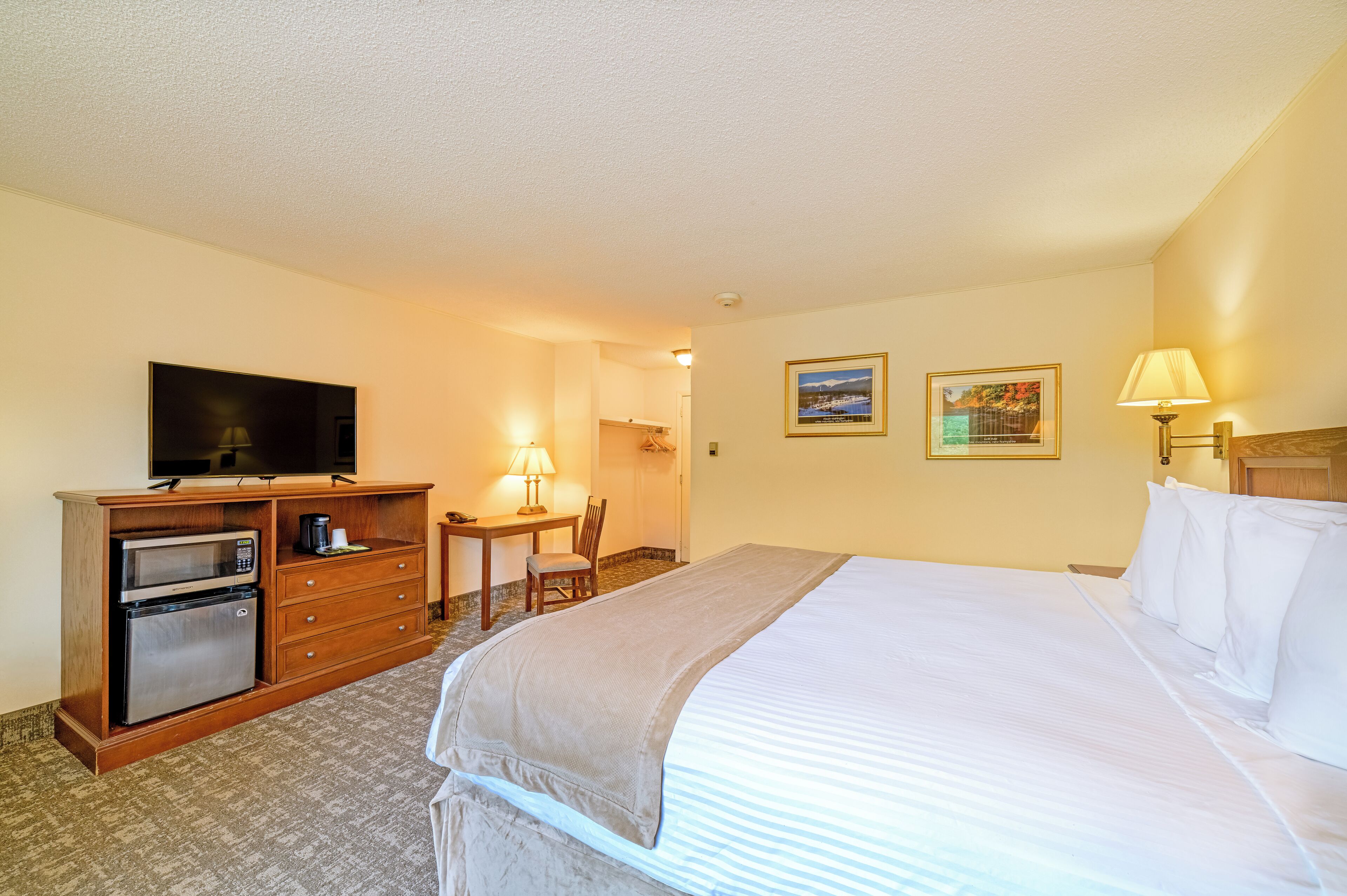 A hotel room with a bed, a desk with a lamp, a television, and a mini-fridge.