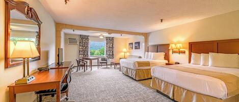 A hotel room with a desk, two beds, a mirror, and a view of the outdoors.