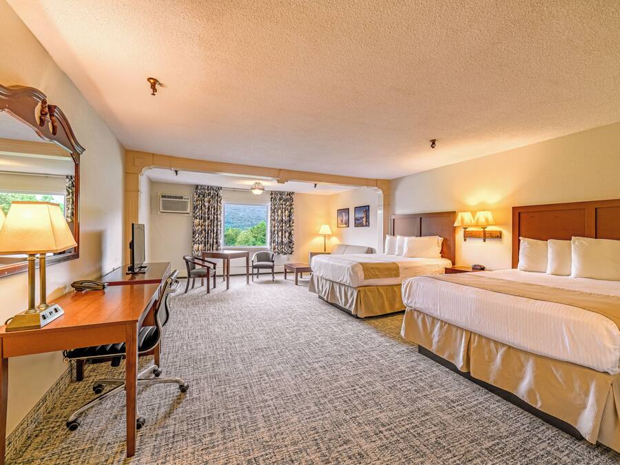 A hotel room with a desk, two beds, a mirror, and a view of the outdoors.