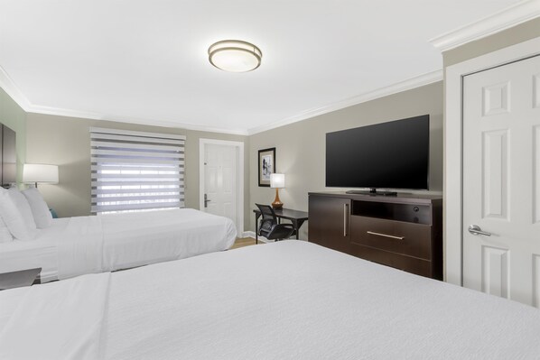 A hotel room with two beds, a desk with a chair, a flat-screen TV, and a wardrobe.