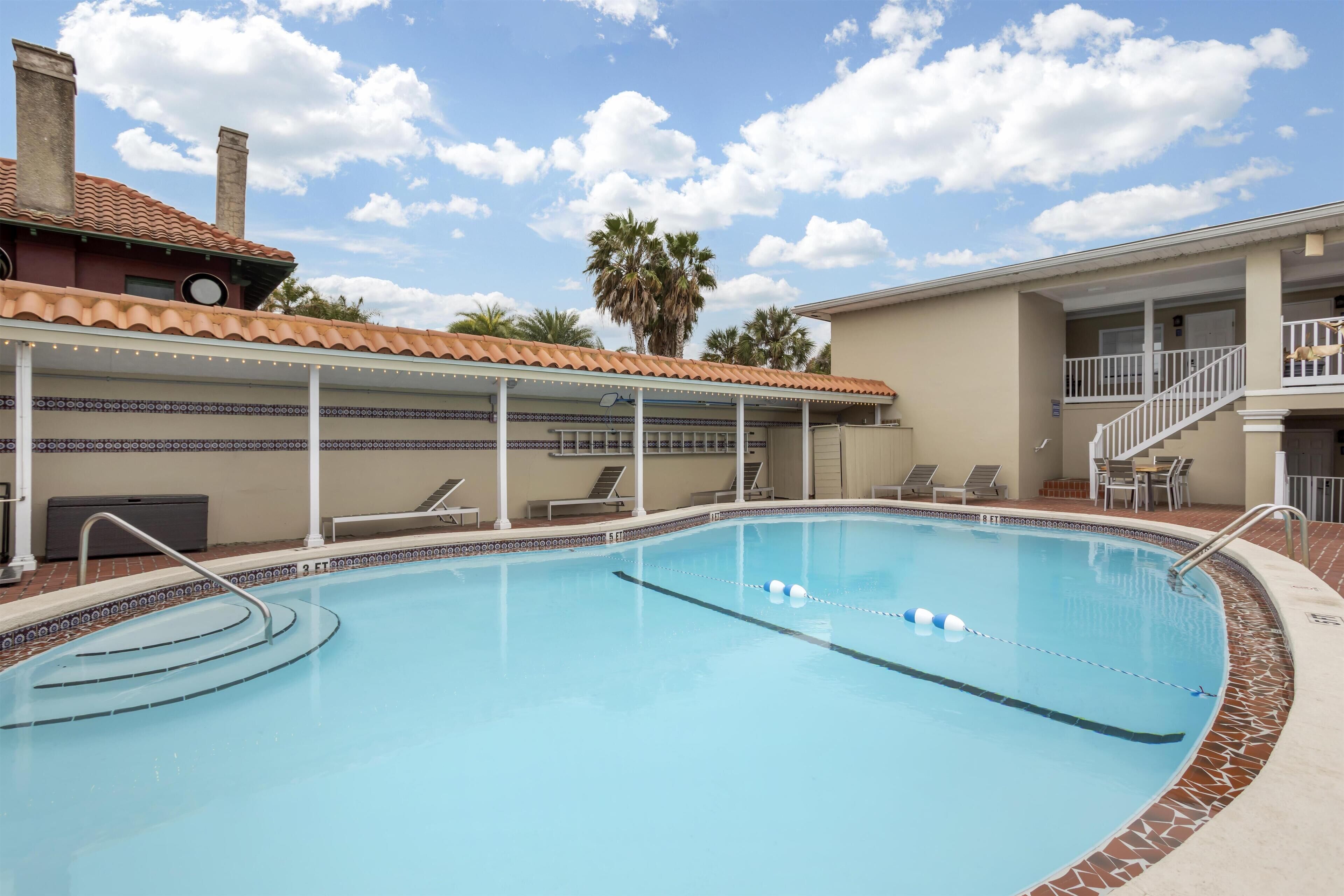 A swimming pool with a tiled deck, lounge chairs, and a covered area with string lights.