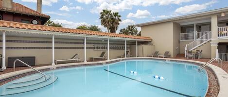 A swimming pool with a tiled deck, lounge chairs, and a covered area with string lights.