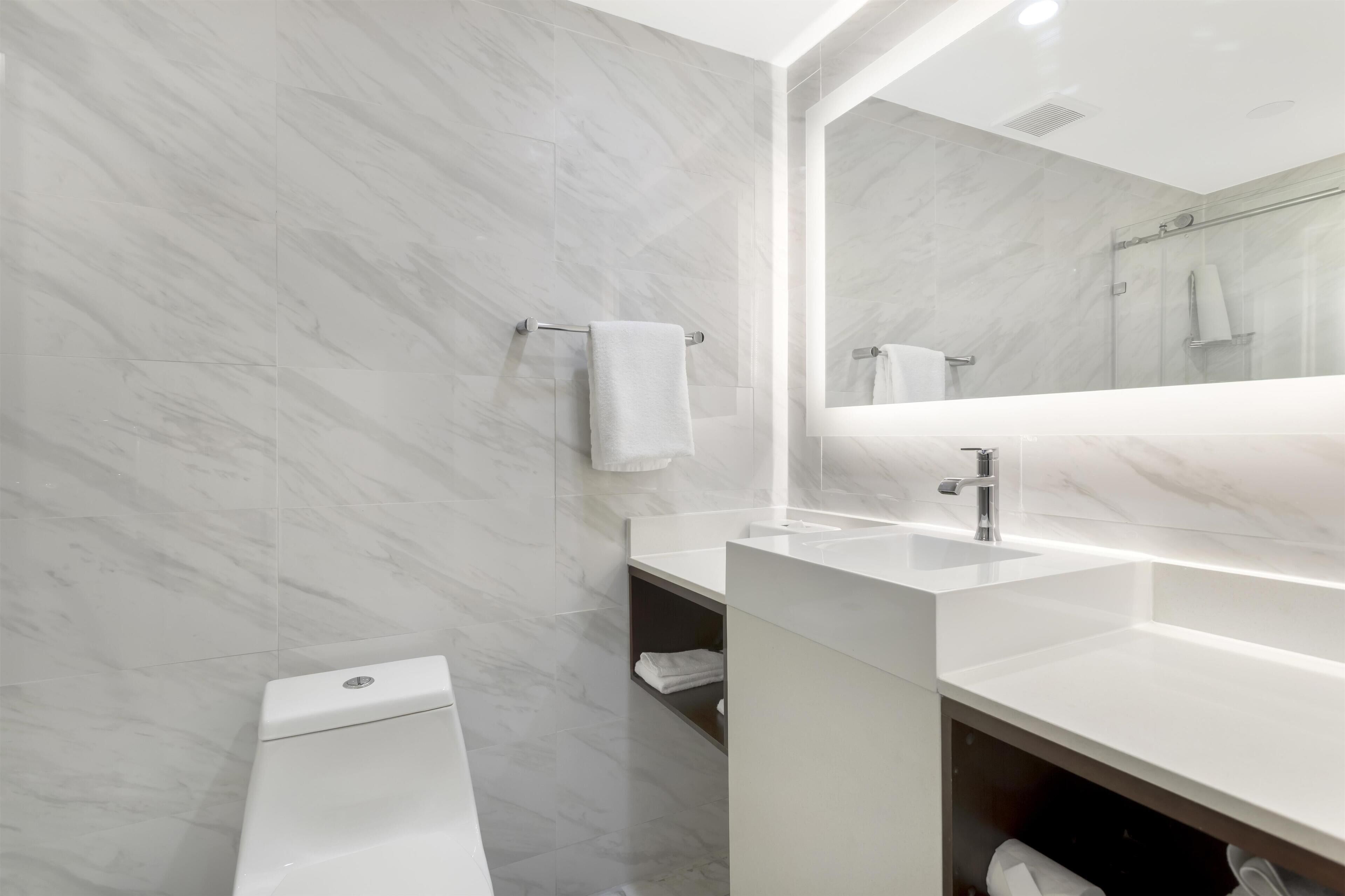 Un baño moderno con pared de mármol, un espejo grande y un lavamanos blanco.