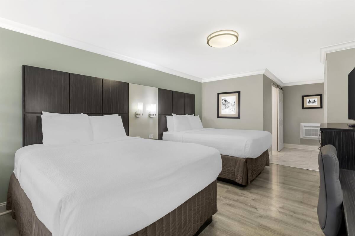 A hotel room with two beds, a desk, and a chair.