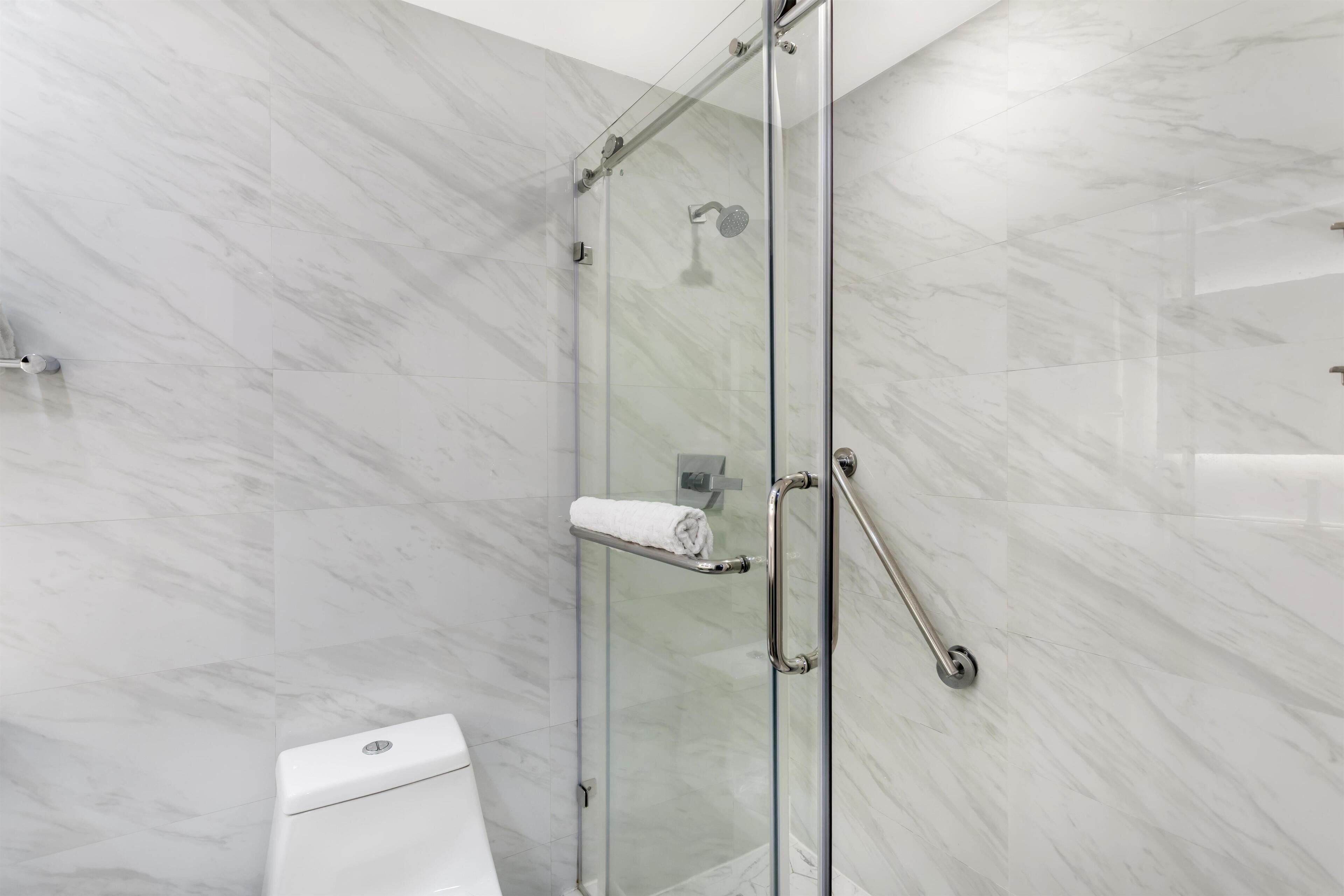 A modern bathroom with a glass-enclosed shower, marble walls, and a white toilet.