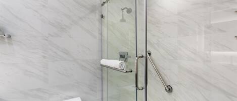 A modern bathroom with a glass-enclosed shower, marble walls, and a white toilet.