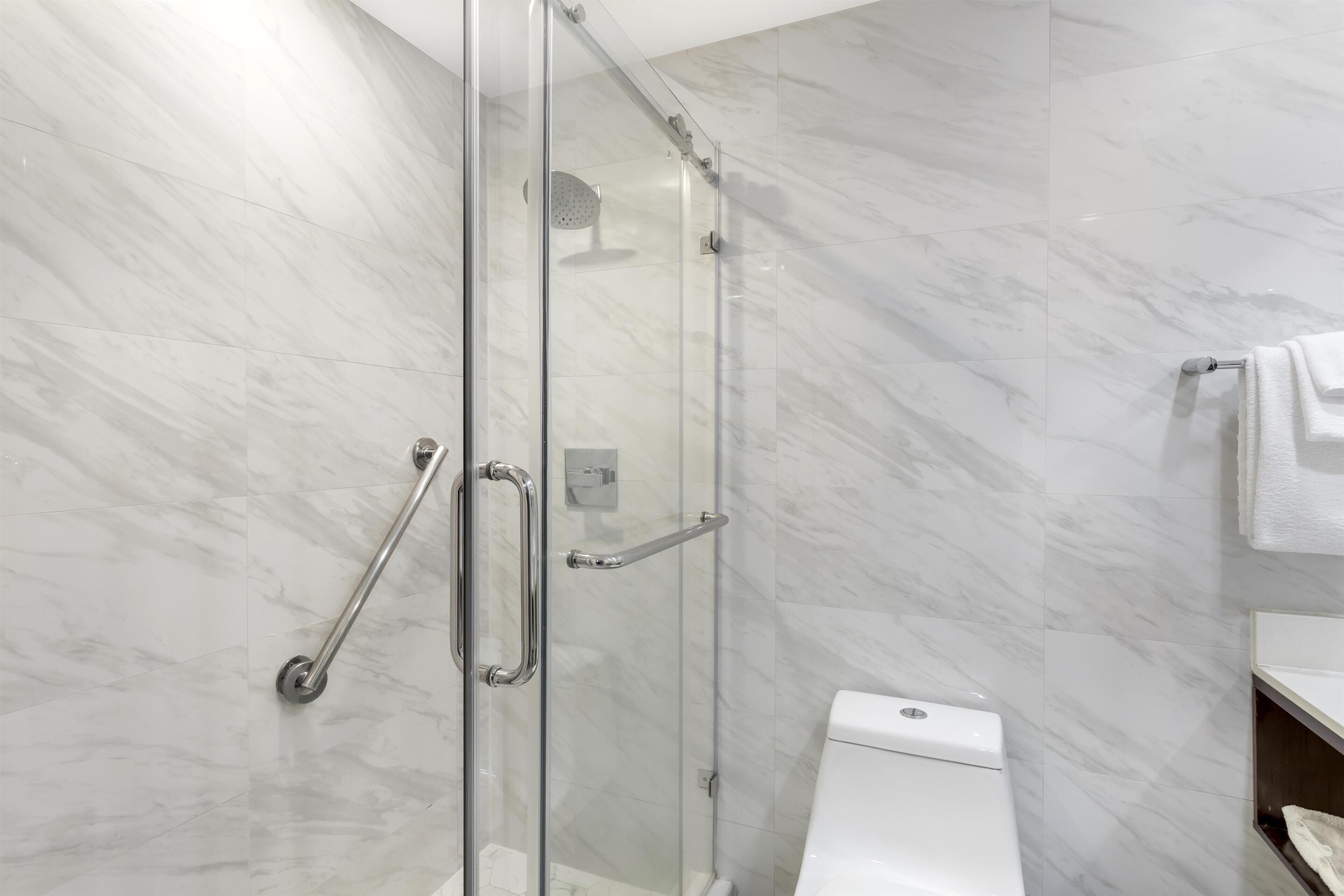 A modern bathroom with a glass shower enclosure, a white toilet, and a towel rack.