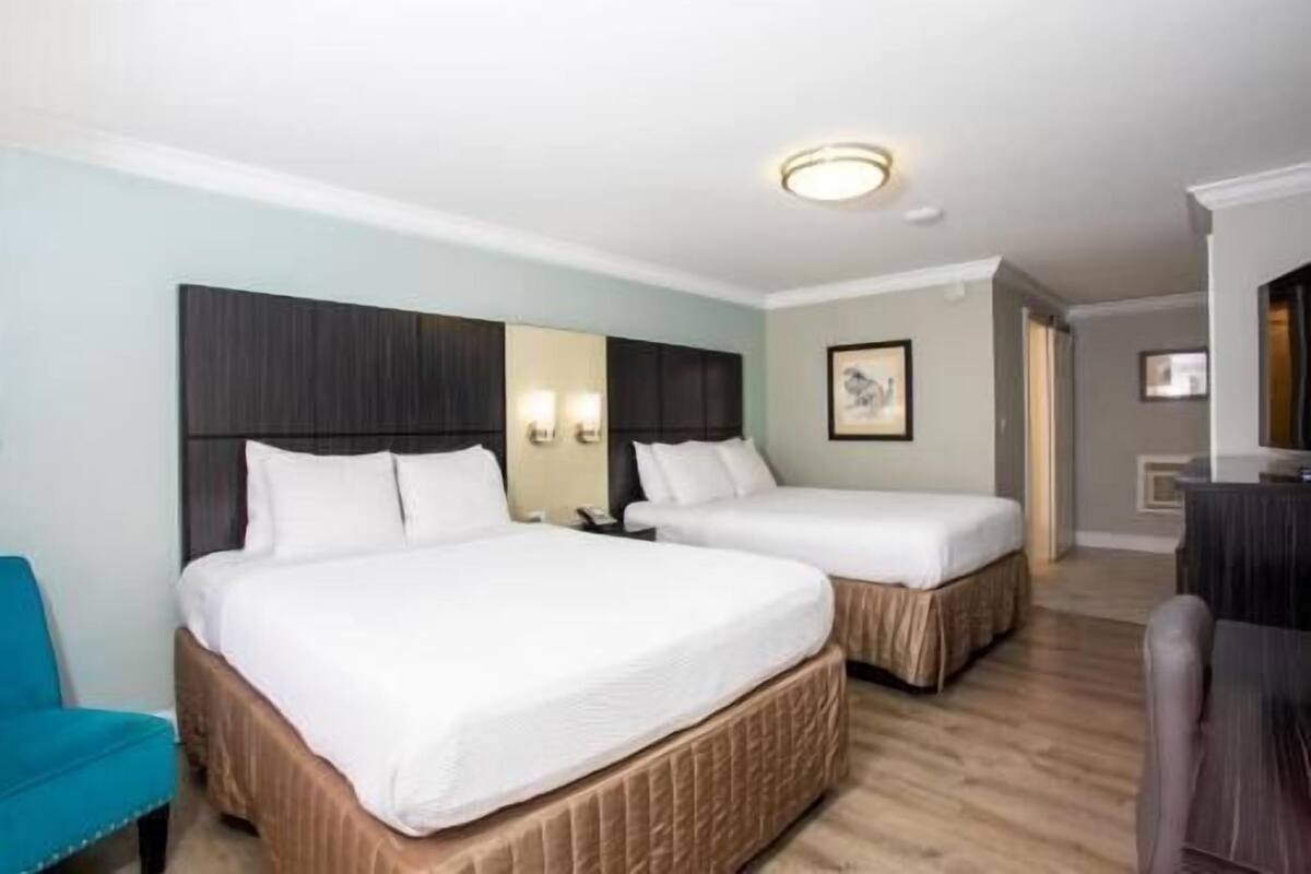 A hotel room with two beds, a blue chair, a desk, and a painting on the wall.