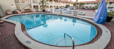 A swimming pool with a brick border, a metal ladder, and a covered umbrella.