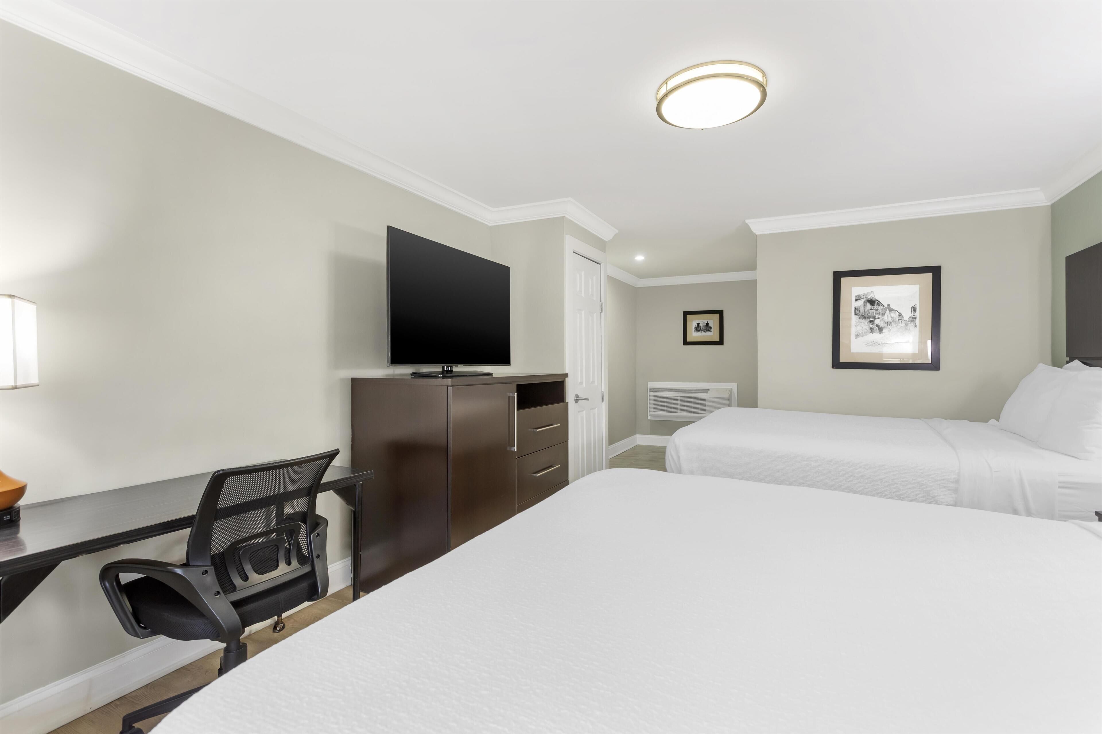 A hotel room with a bed, a desk with a chair, a television, and a framed picture on the wall.