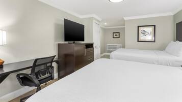 A hotel room with a bed, a desk with a chair, a television, and a framed picture on the wall.