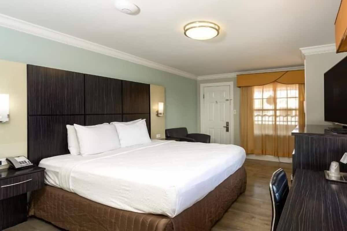 A hotel room with a bed, bedside table, desk, chair, TV, and a door leading to a balcony.