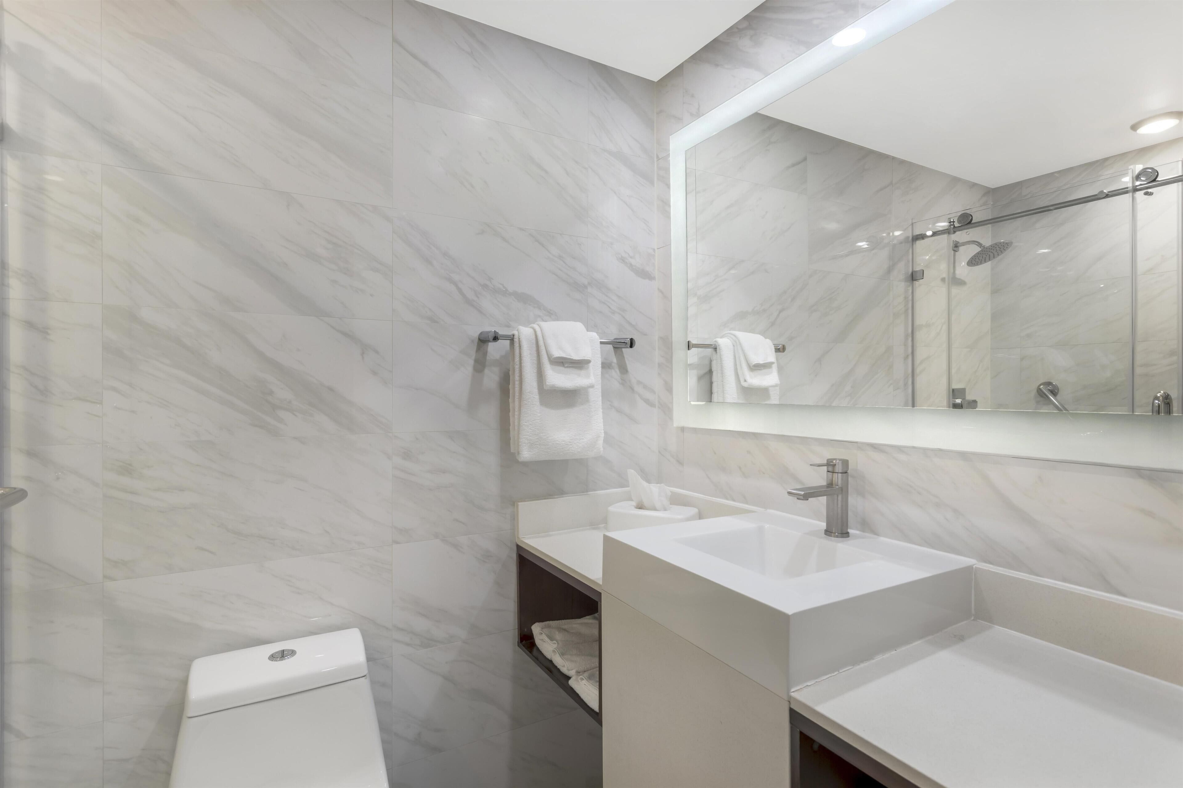 A modern bathroom with marble walls, a toilet, a sink, and a shower area.