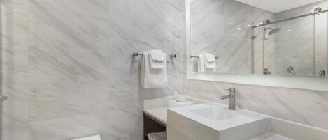 A modern bathroom with marble walls, a toilet, a sink, and a shower area.