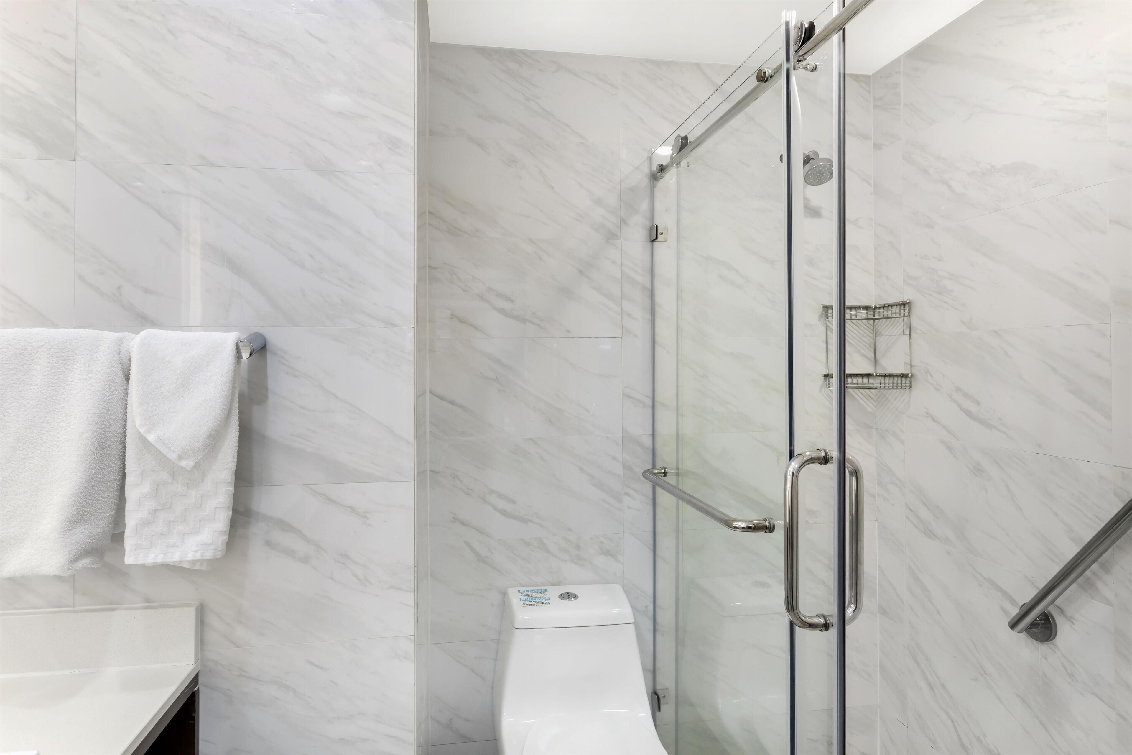 Un baño moderno con cabina de ducha de vidrio, inodoro blanco y toallero con dos toallas.