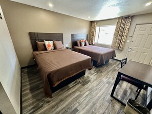 A hotel room with two beds, a wooden floor, a desk, and a window with curtains. - West Inn NAU - Downtown Flagstaff (Flagstaff)