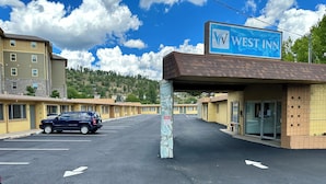 Un motel de la cha îne West Inn, avec un parking, une enseigne bleue et une rangée de chambres de motel.