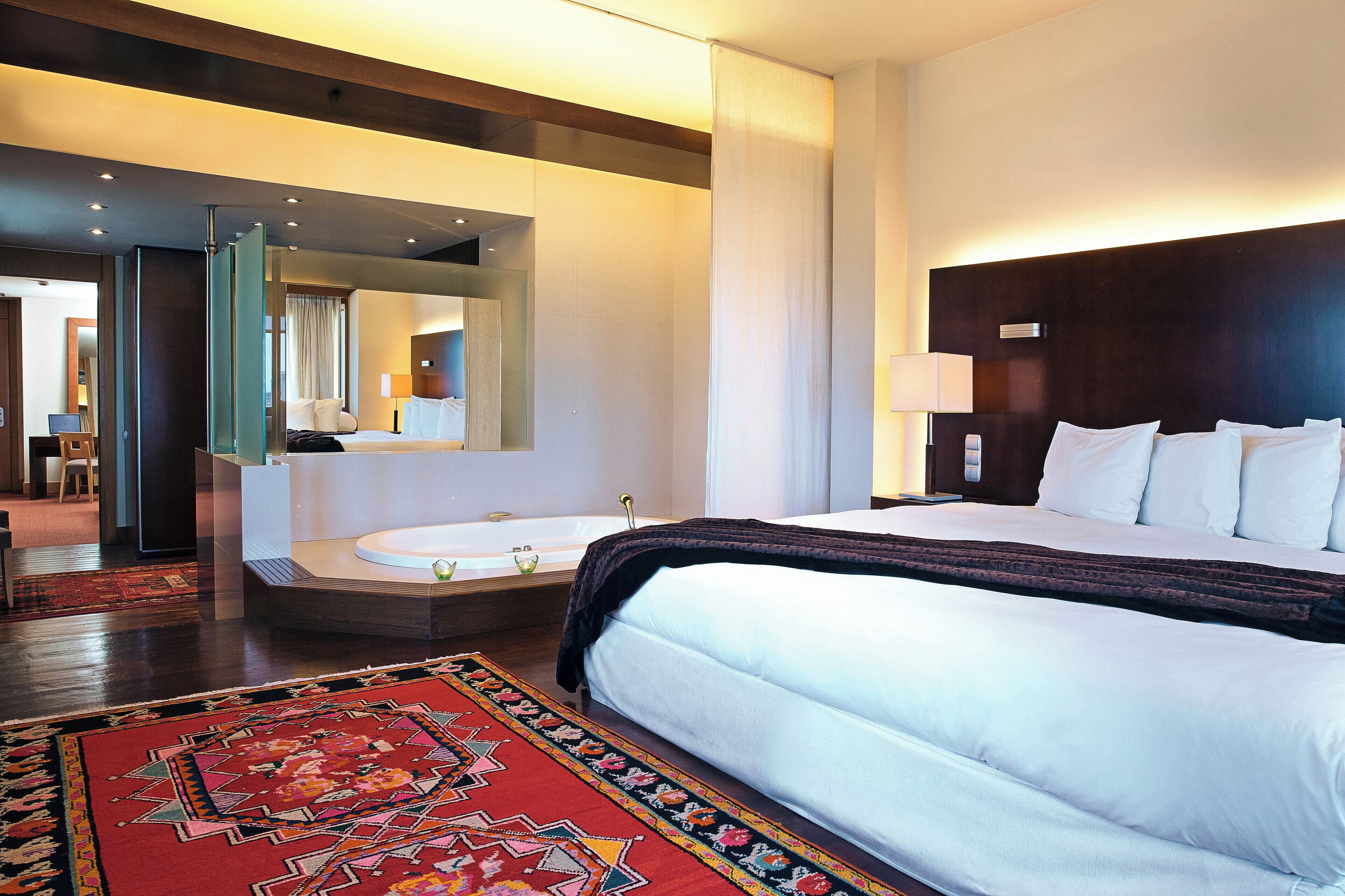 Ein Hotelzimmer mit einem großen Bett, einer Sitzecke mit einem Sessel, einer Badewanne und einem großen Spiegel.