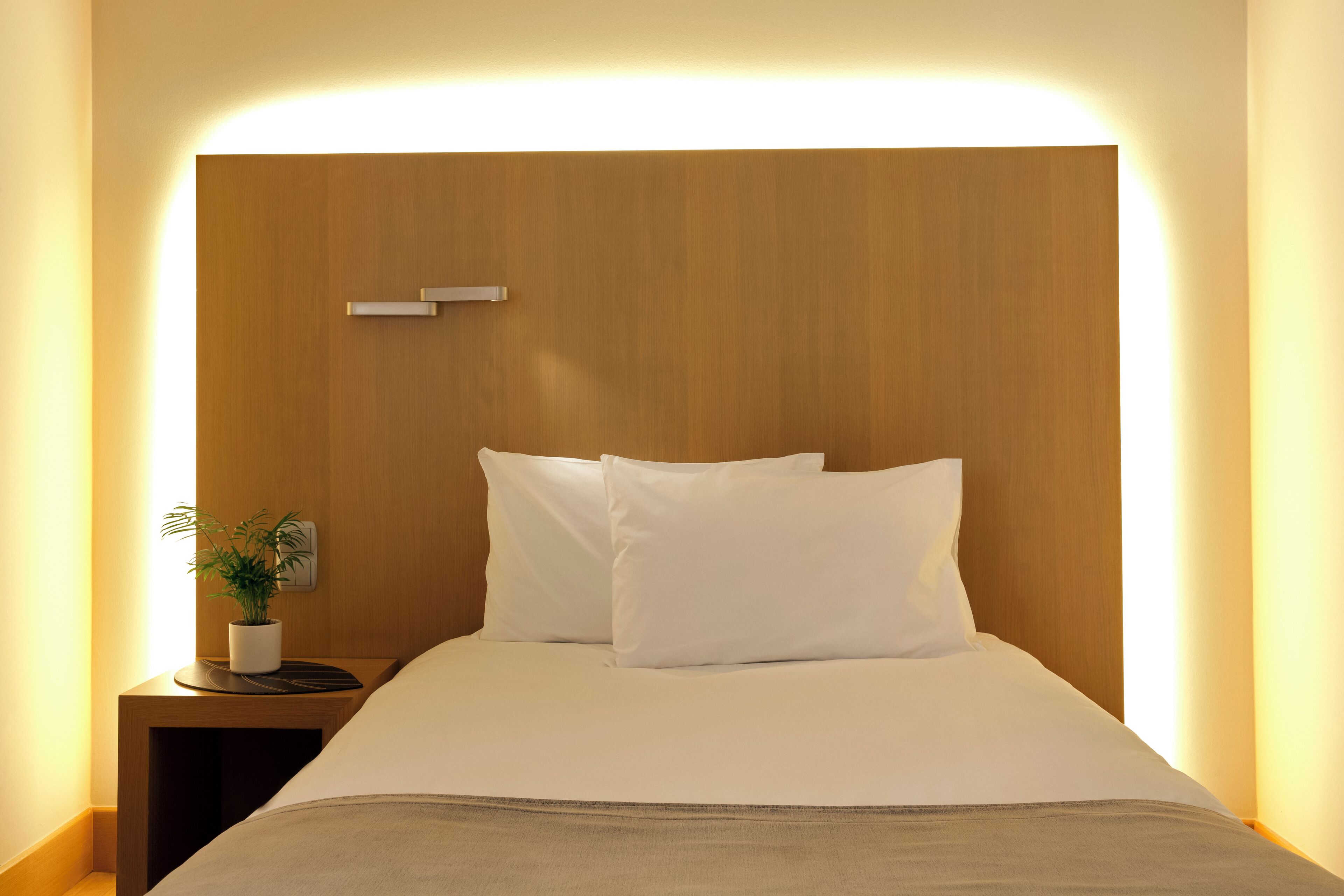 A neatly made bed with white linens and a wooden headboard.