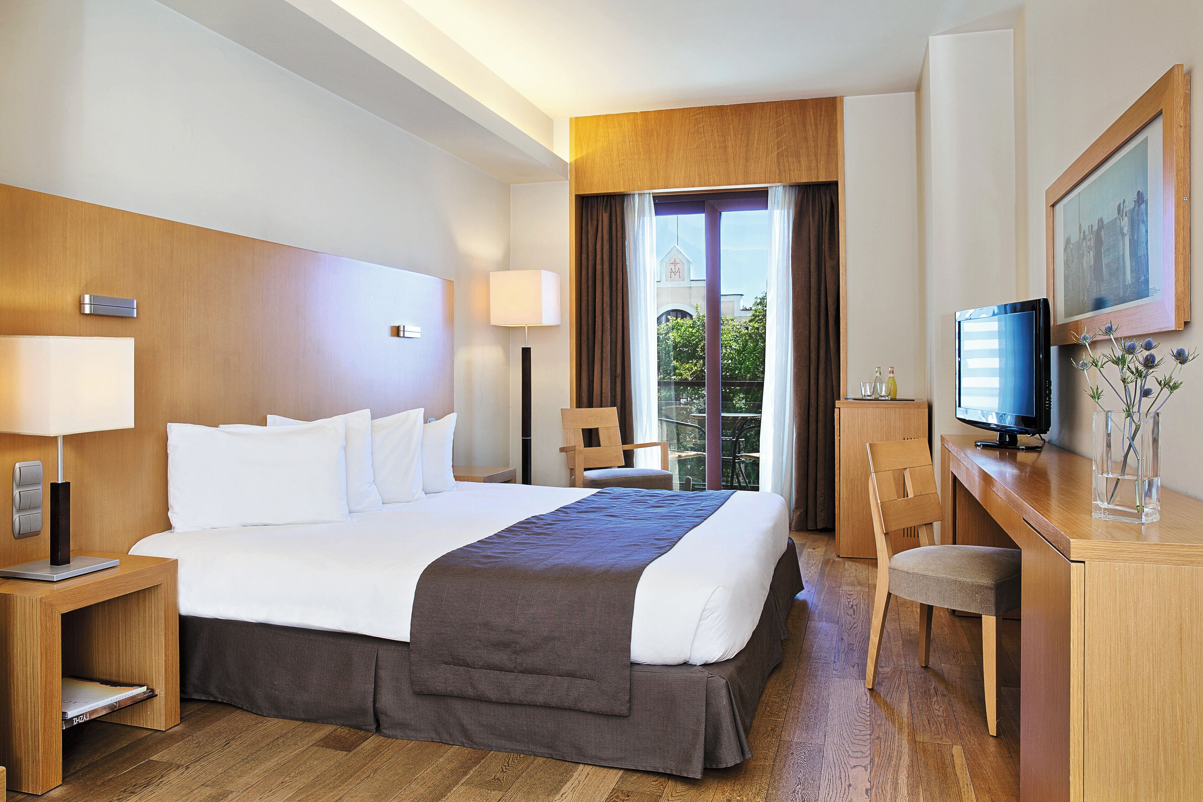 A hotel room with a large bed, a desk with a computer, a chair, and a television.