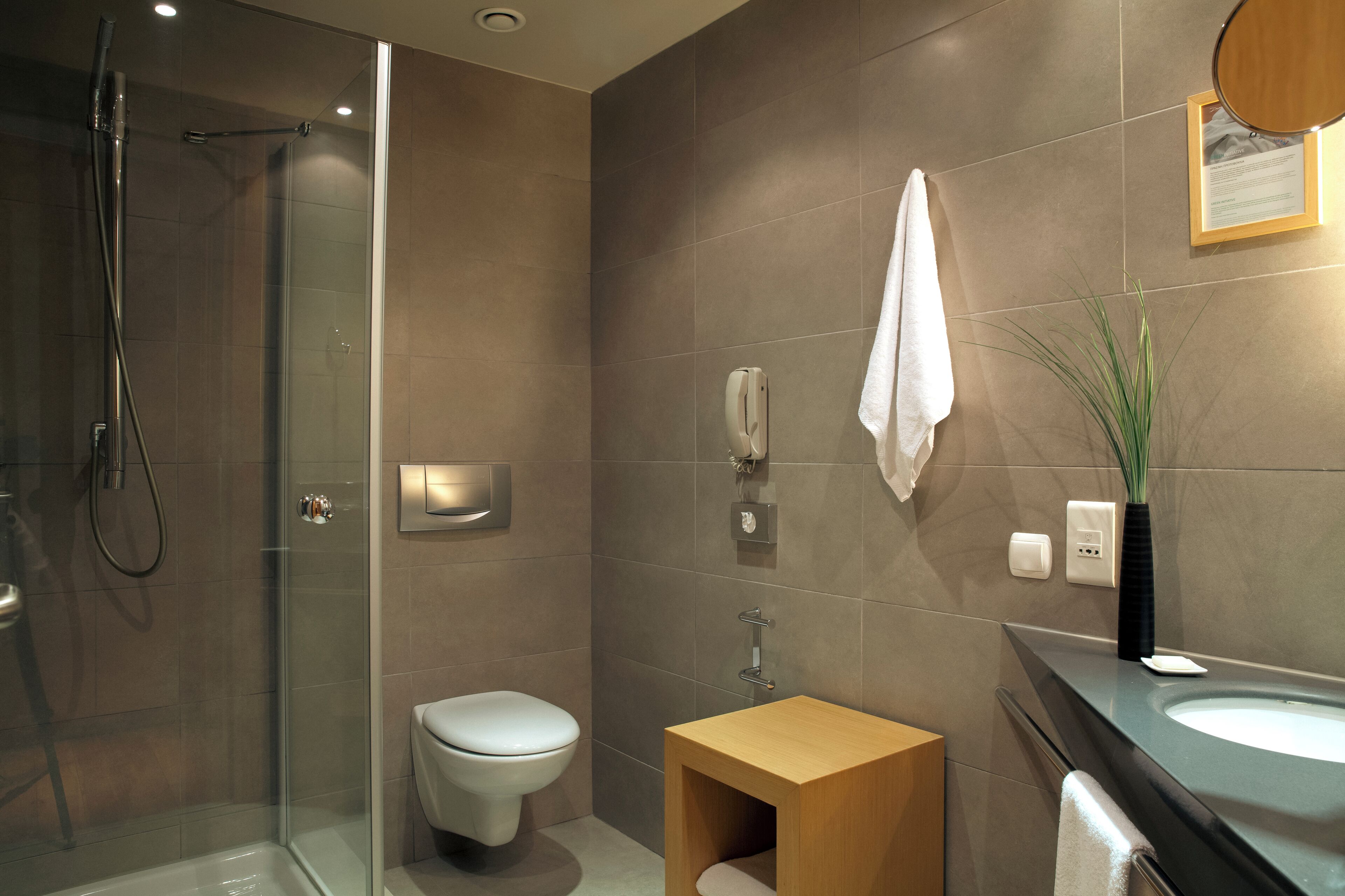 Un baño moderno con ducha de vidrio, inodoro, tocador de madera y lavamanos con espejo.