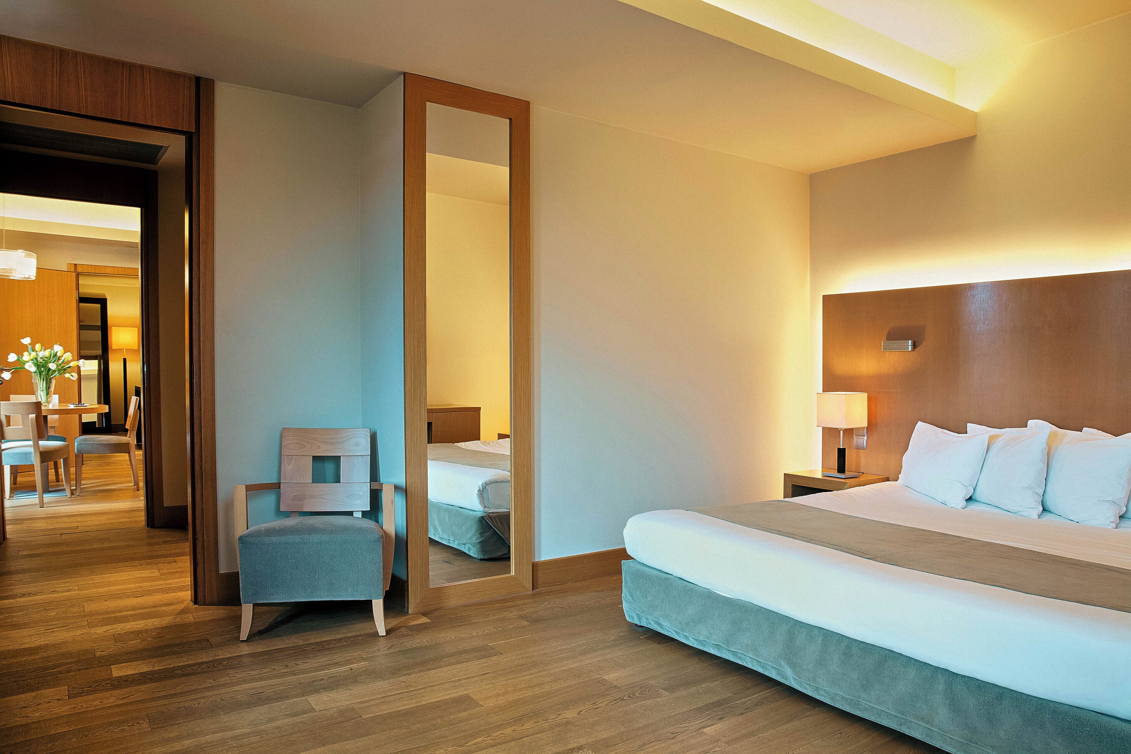 A hotel room with a large bed, a chair, a desk, and a mirror.