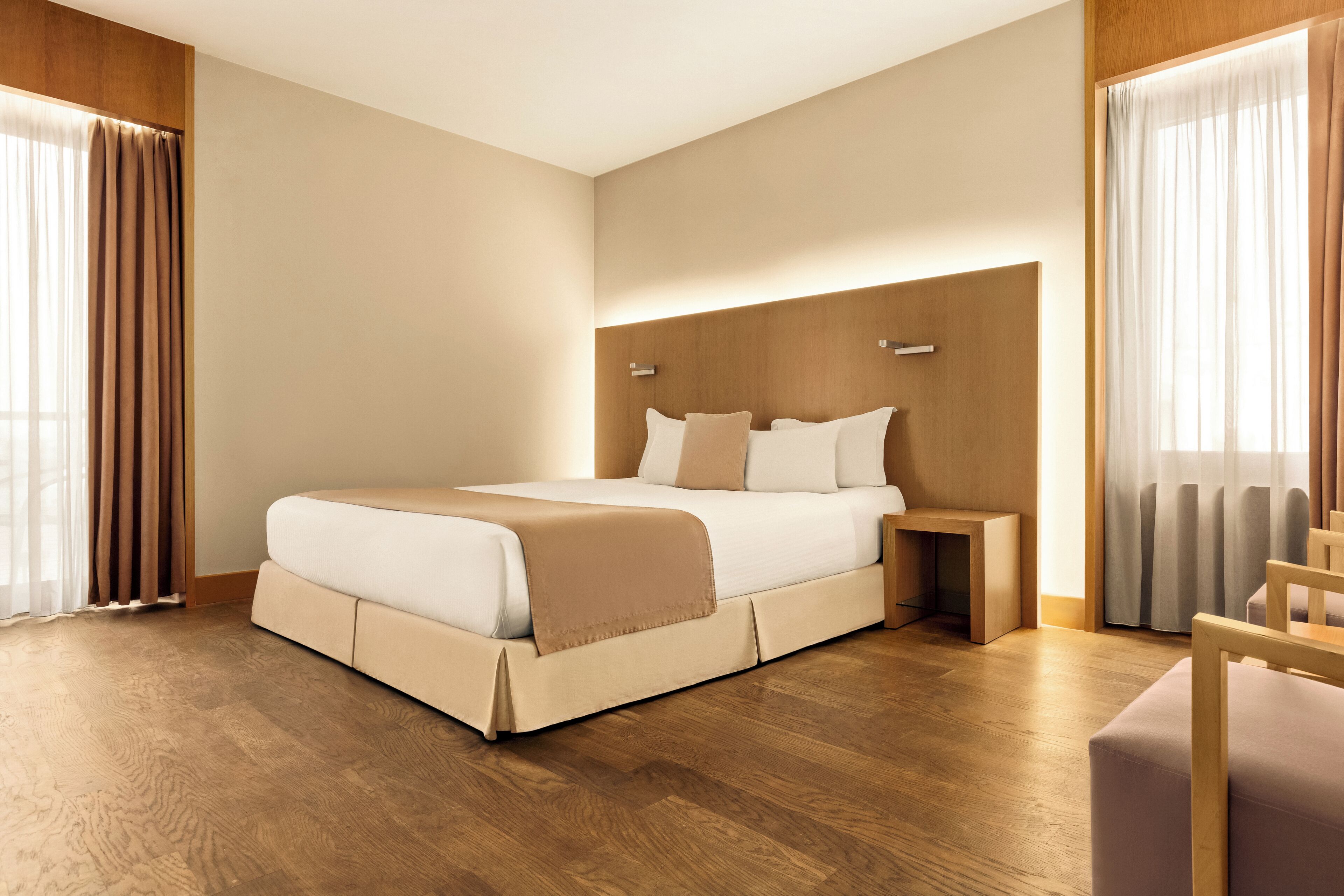 A modern hotel room with a large bed, wooden flooring, a headboard, and a nightstand.