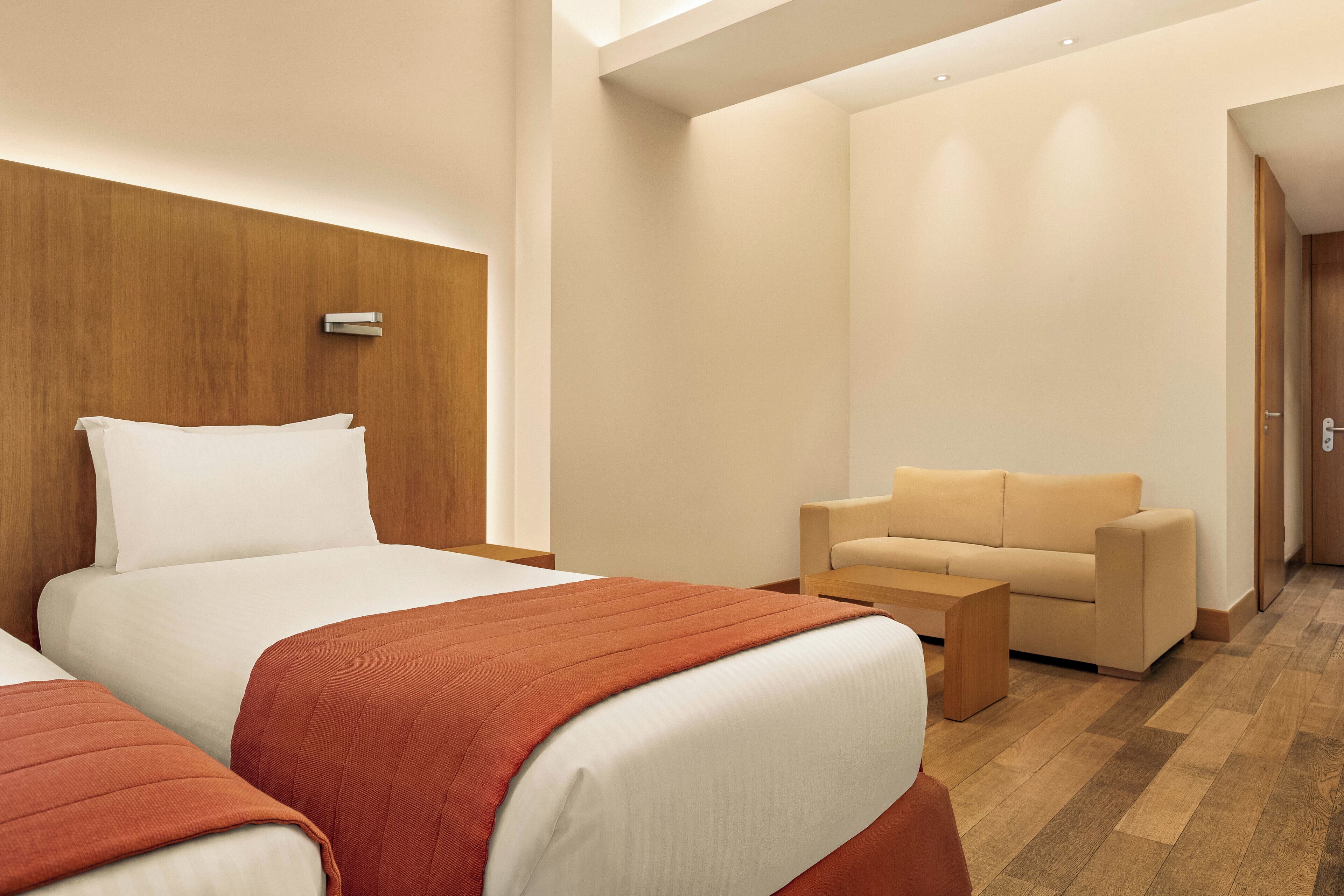 Habitación de hotel con dos camas, un sofá y un cabecero de madera.