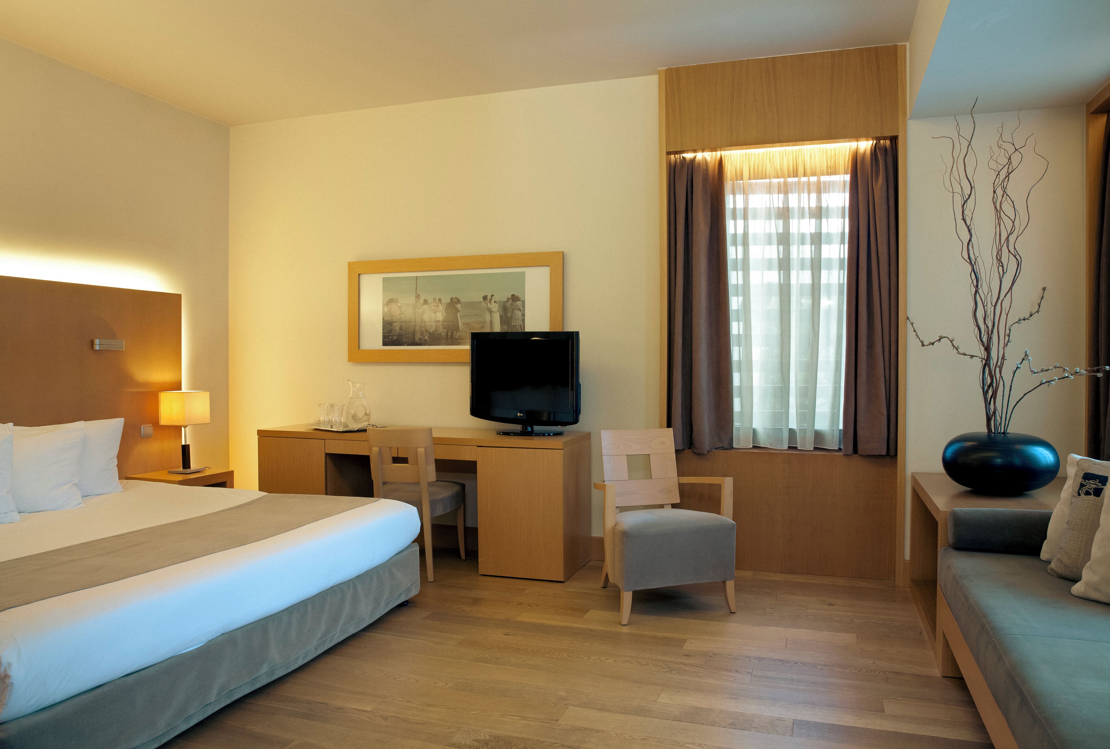 Una habitación de hotel con cama, escritorio, silla, televisor y ventana con cortinas.