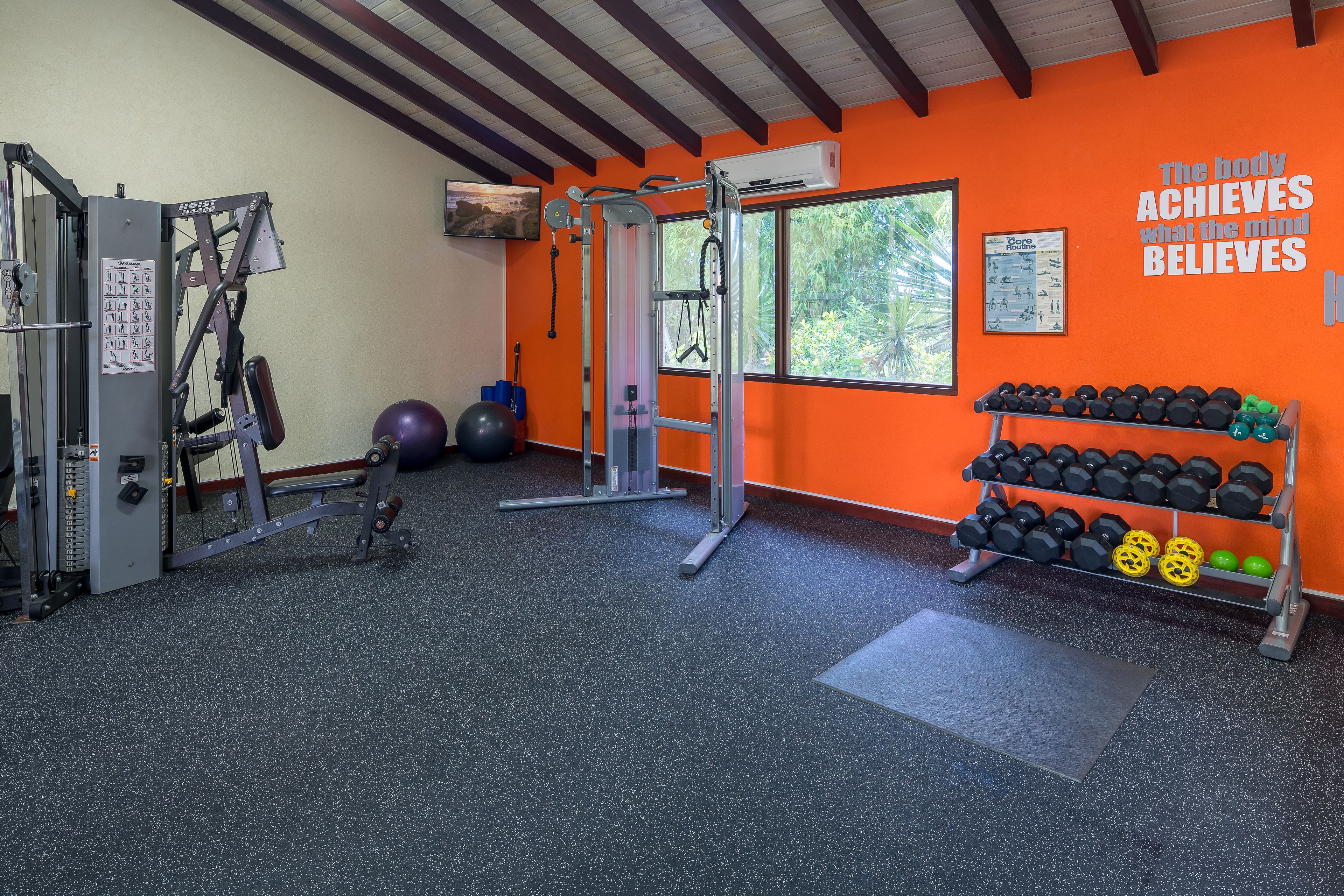 A gym with exercise equipment, a rack of dumbbells, and a motivational quote on the wall.