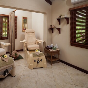 A spa room with two massage chairs, a small table with bottles, and a window with blinds.