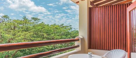 A balcony with a wooden railing, a small round table, and a wicker chair.