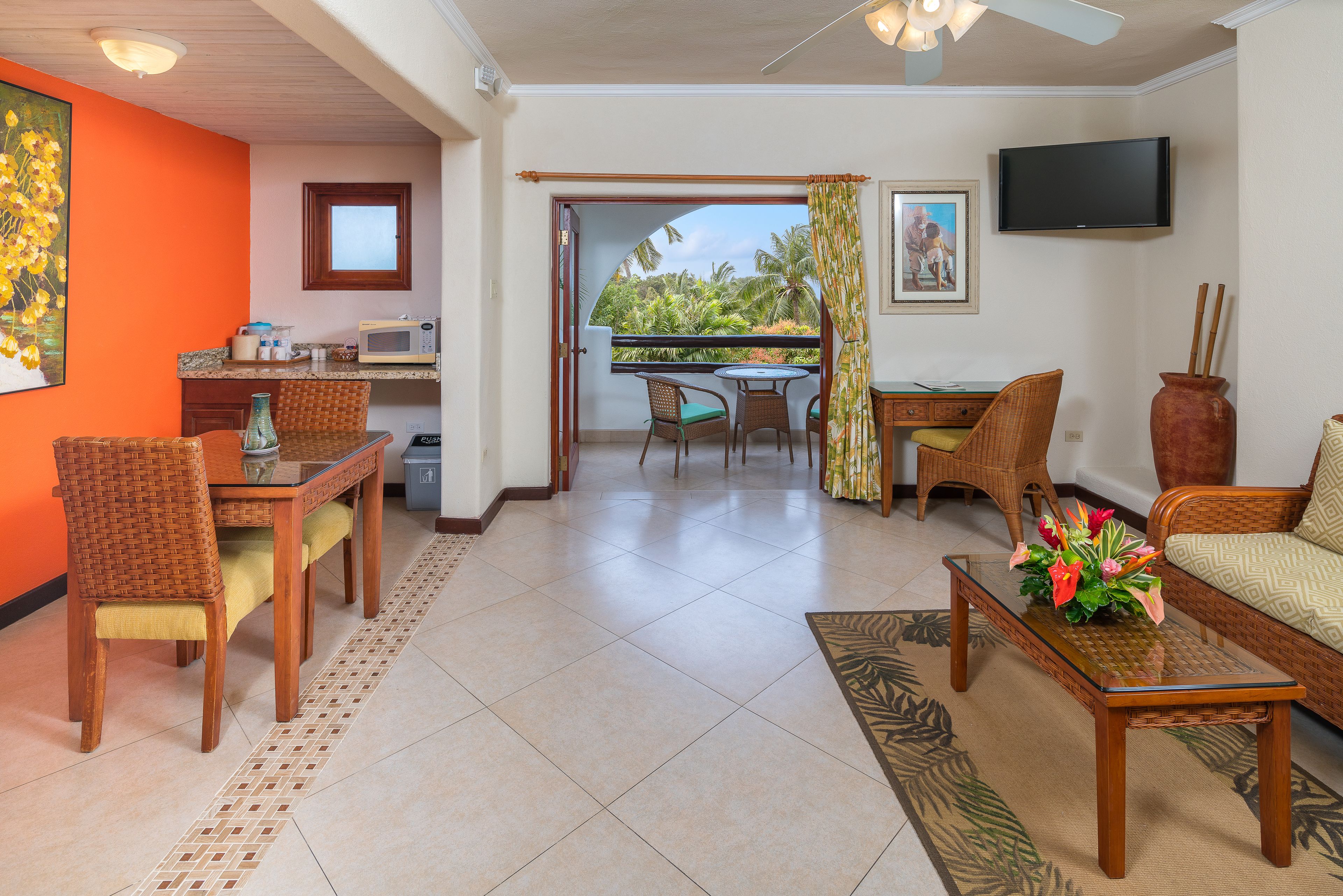A living room with a dining area, a TV mounted on the wall, and a view of the outdoors.